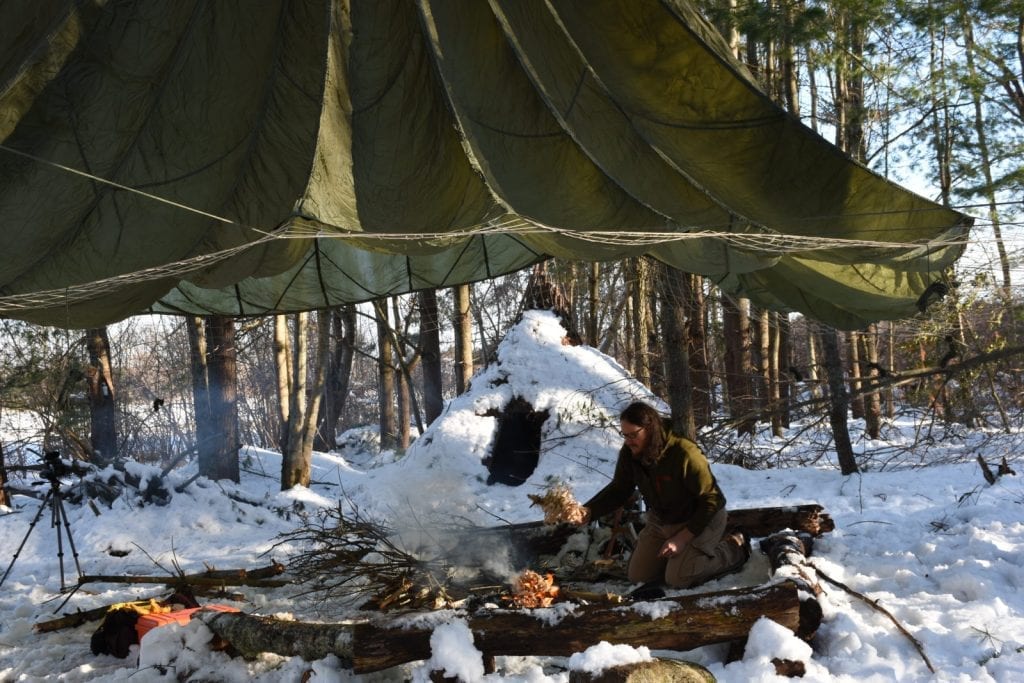 man in a snow lighting up a campfire 