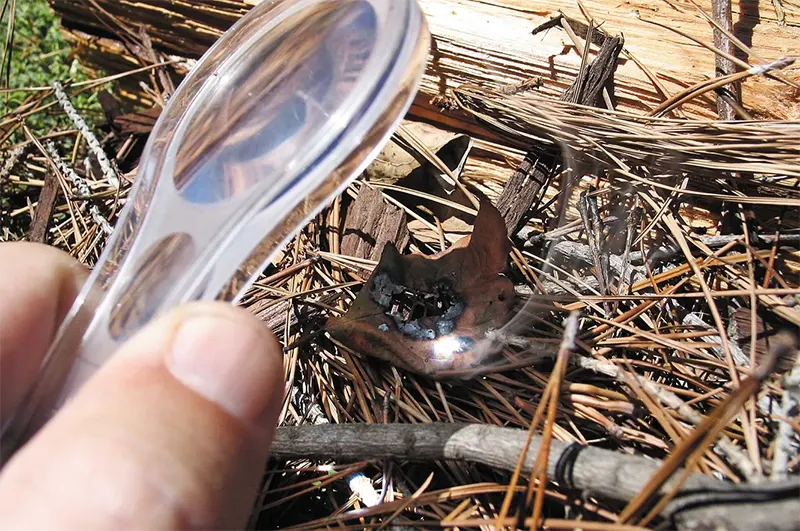 creating a fire using a magnifying glass and a dead leaf and branches