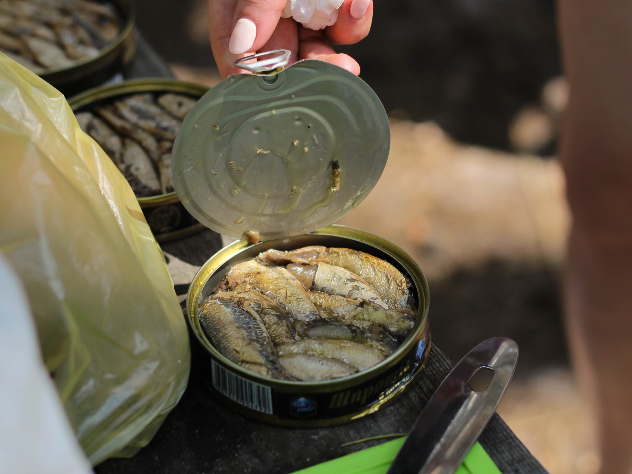 A hand opening a new can of tuna fish beside other opened tuna cans. 