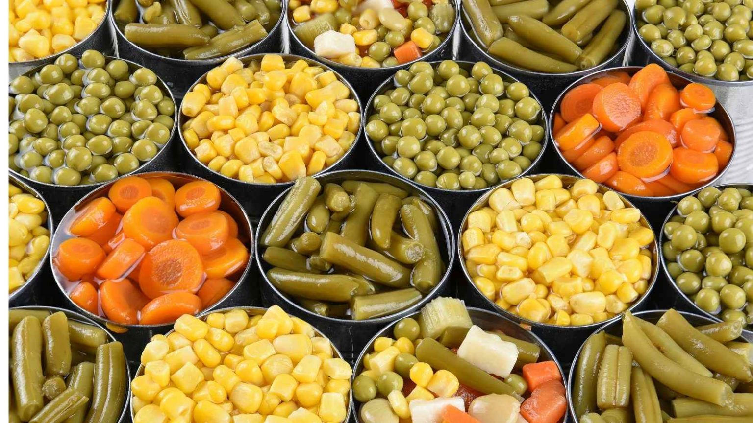 Newly-opened cans of canned vegetables including canned beans, carrots, corn, and pickles. 