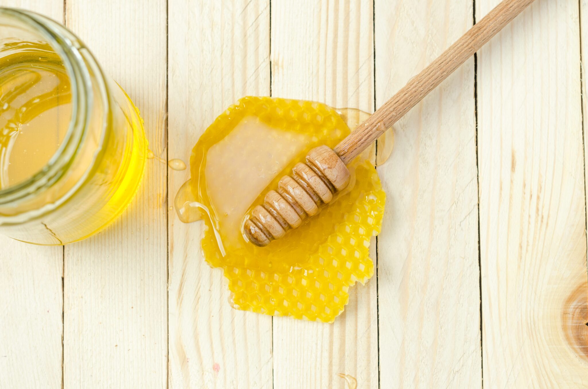 A glass of honey and some honey spillage beside the honey dipper on the wood table. 