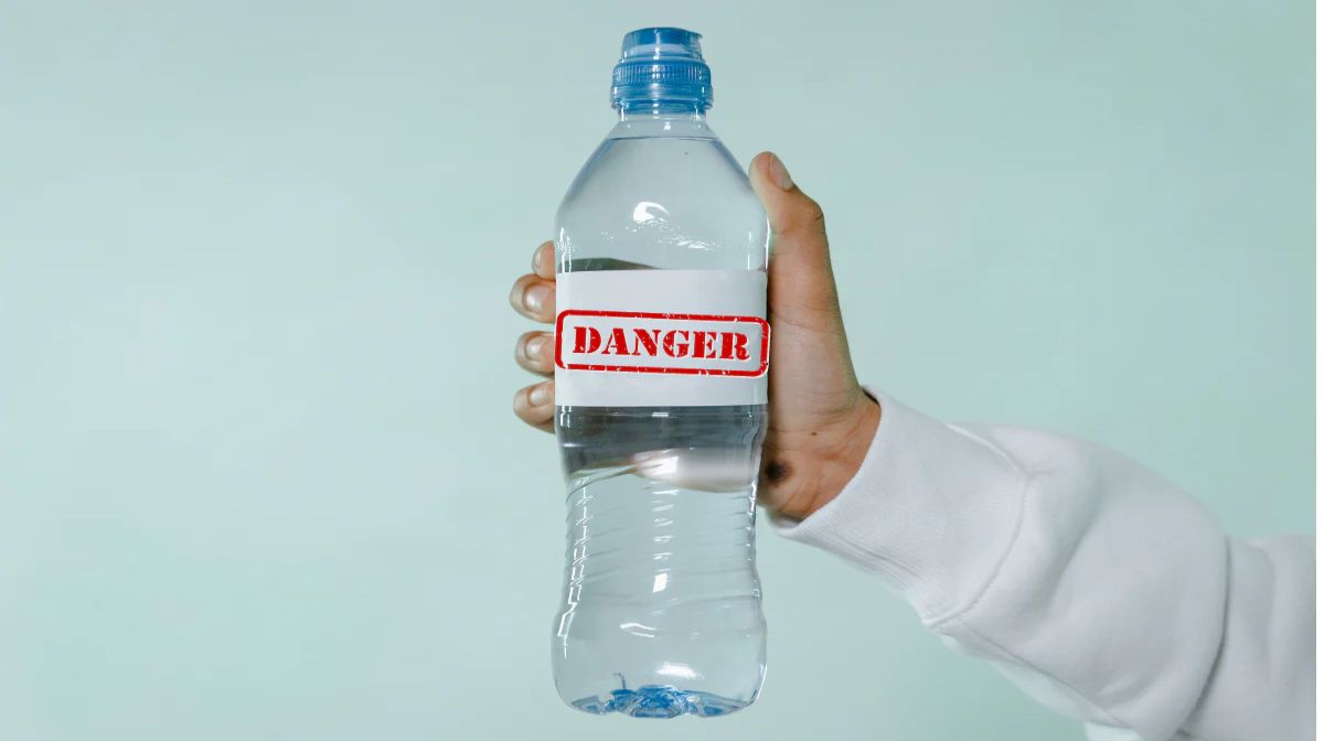 A hand holding a plastic bottled water with a "danger" sign. 