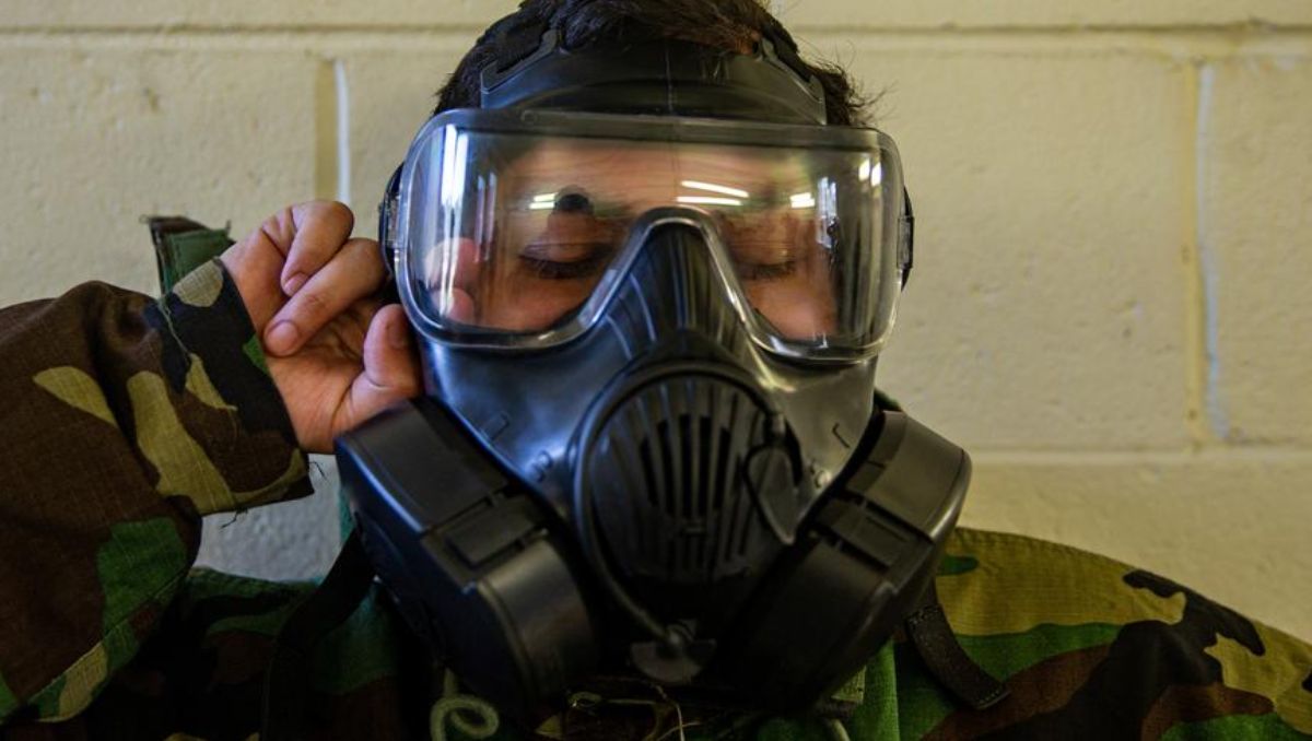 A military guy doing a seal check on his gas mask.